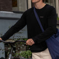 man wearing black merino wool longsleeve while walking with bike in his hand
