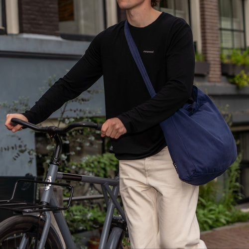 man wearing black merino wool longsleeve while walking with bike in his hand